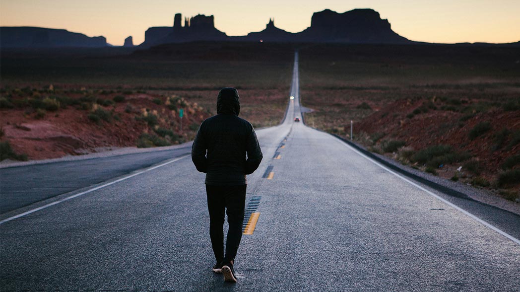 Color photo of a jogger running through Monument Valley, Utah at sunrise or sunset.